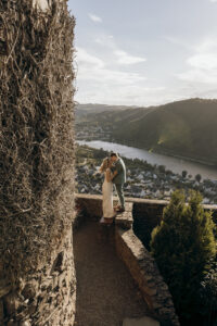 Ein romantischer Moment zwischen einem Paar auf einem Turm mit Blick auf ein malerisches Flusstal bei Sonnenuntergang, festgehalten von ihrem Hochzeitsfotografen während ihres Hochzeitsfotoshootings.